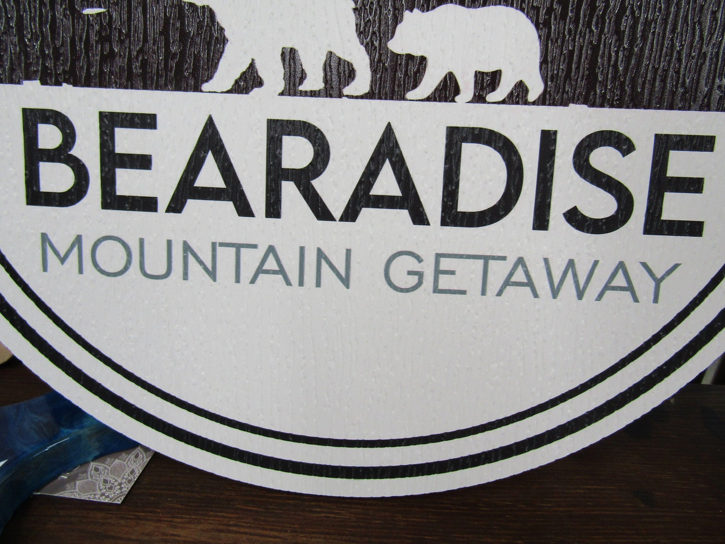 A close up of round sign for Bear's Paradise Mountain Getaway, featuring custom cabin pine trees wilderness bears textured PVC, weather fade resistant, waterproof UV printed color logo business commercial signage