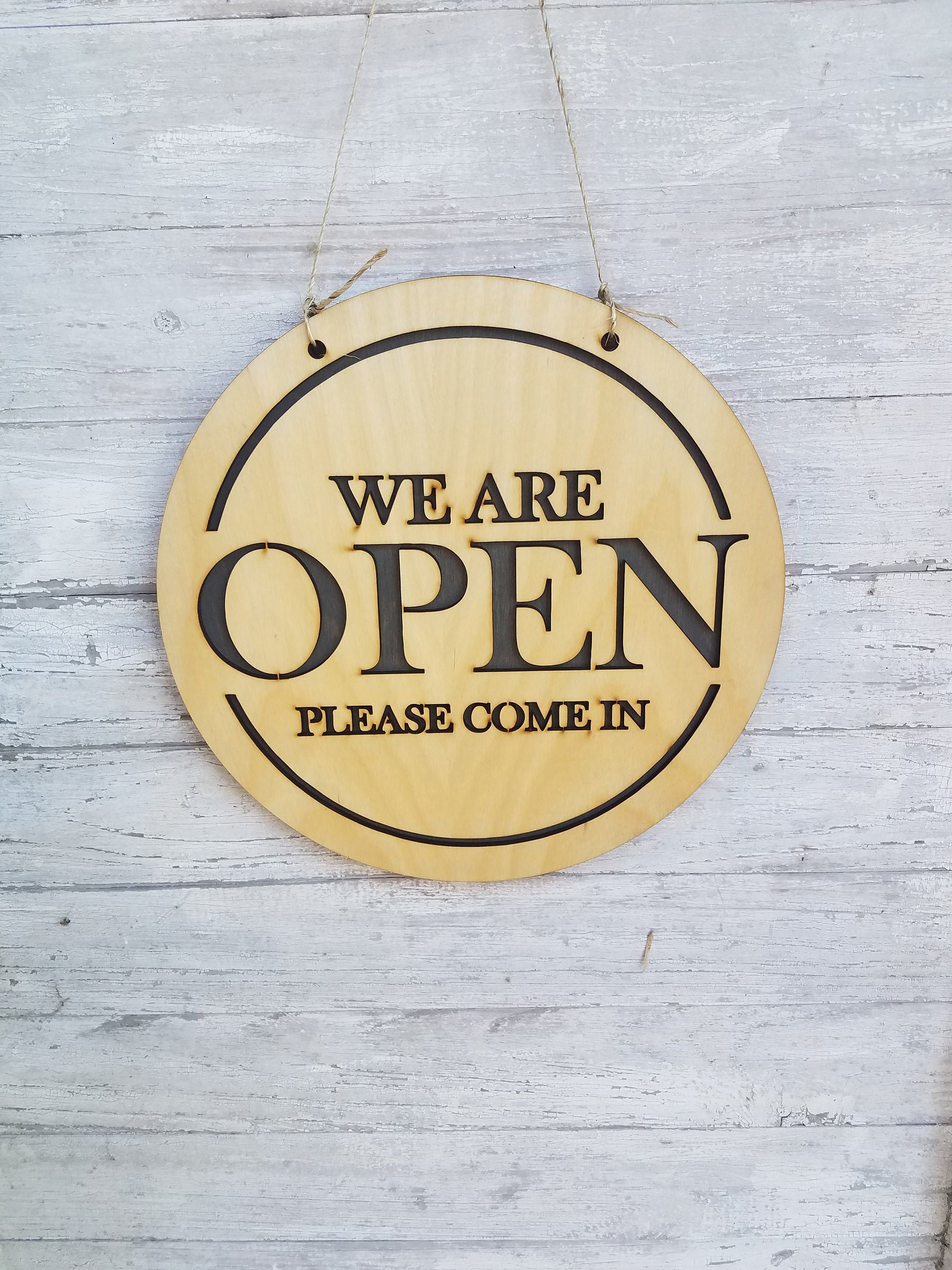 May include: A round wooden sign with the text "We are open. Please come in." in black lettering.